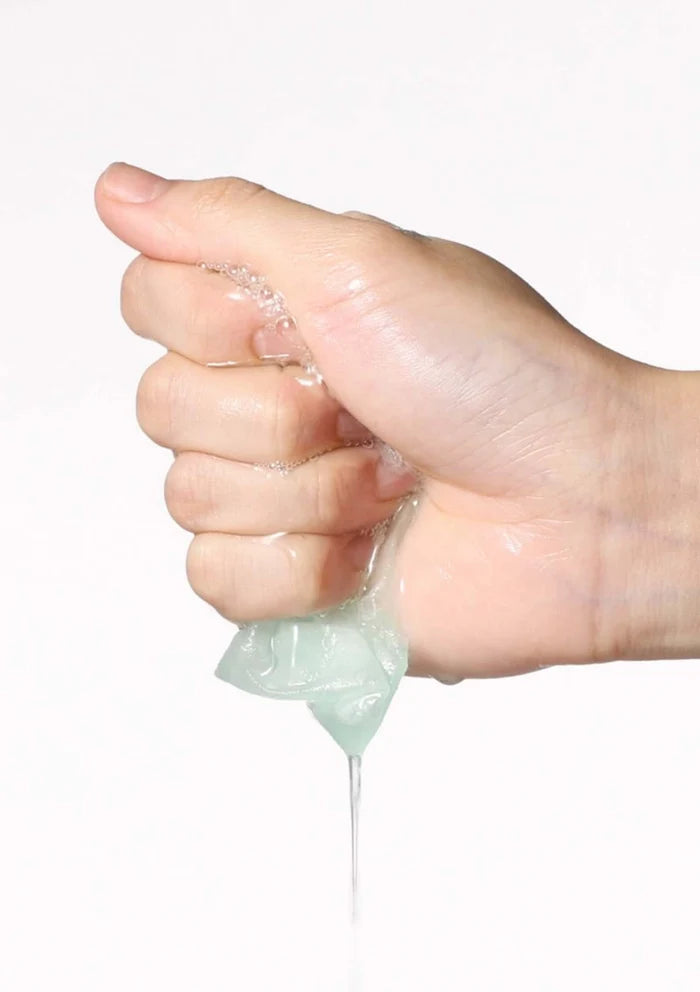 Hand squeezing a small container of clear gel against a white background