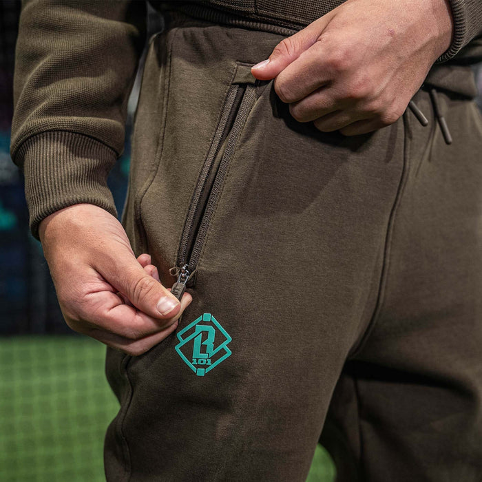 Brown pants with a green BL101 logo on the pocket, held by a person.