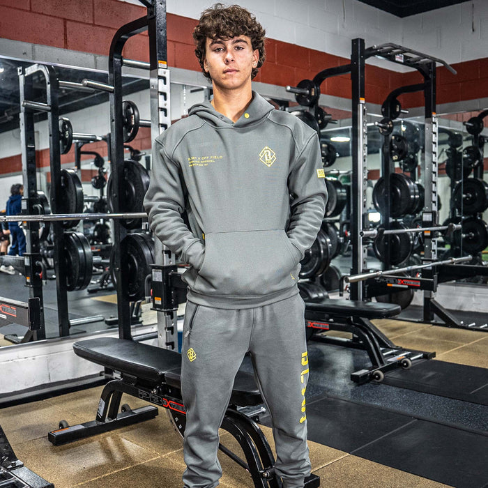 Person wearing a gray tracksuit with yellow BL101 logos in a gym setting