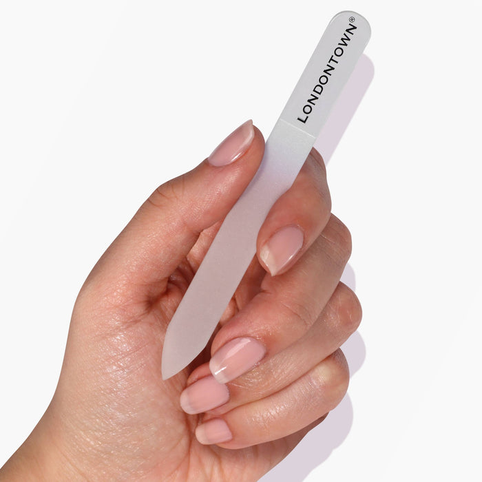 A hand holding a LONDONTOWN Glass Nail File - White against a white background, showcasing effortless and damage-free nail filing.