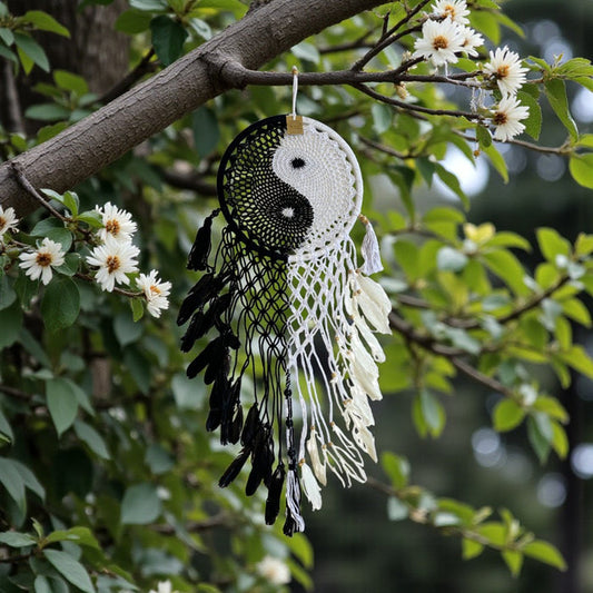 Dreamcatcher with yin yang symbol hanging from a tree branch with flowers.