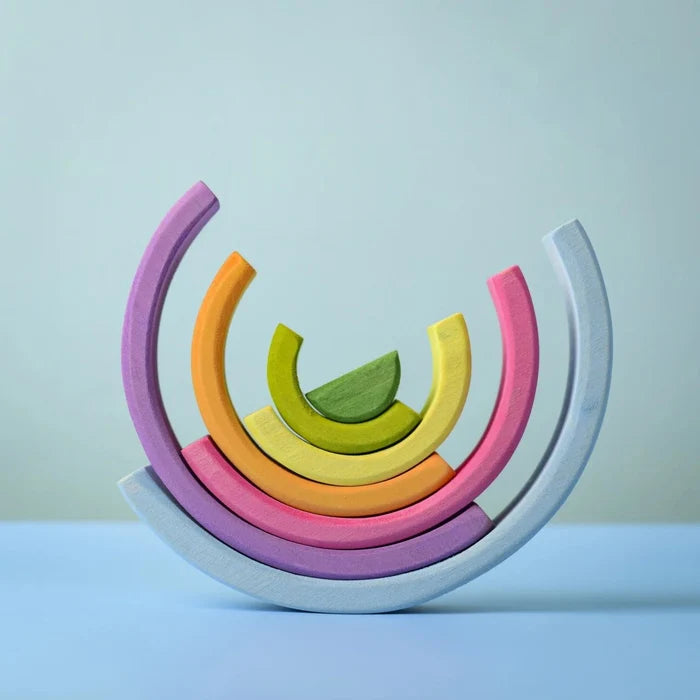 A set of pastel-colored wooden arch blocks arranged in a semi-circular stack on a light blue surface against a pale blue background.