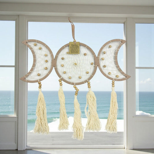 Decorative dreamcatcher with tassels hanging in front of a window with a view of the ocean.
