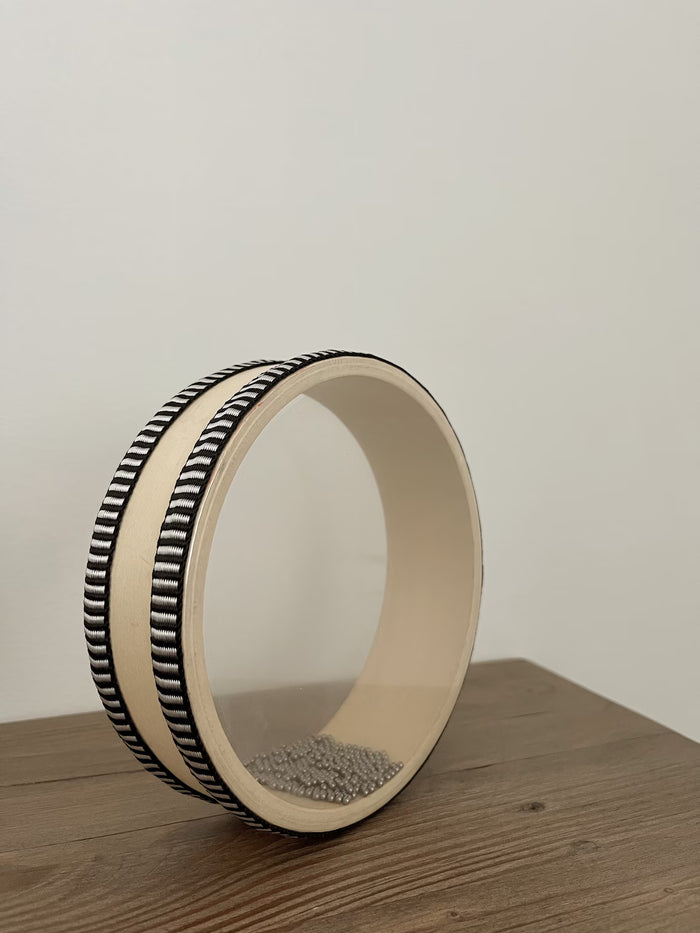 Wooden drum on its side with metal beads inside on a wooden surface
