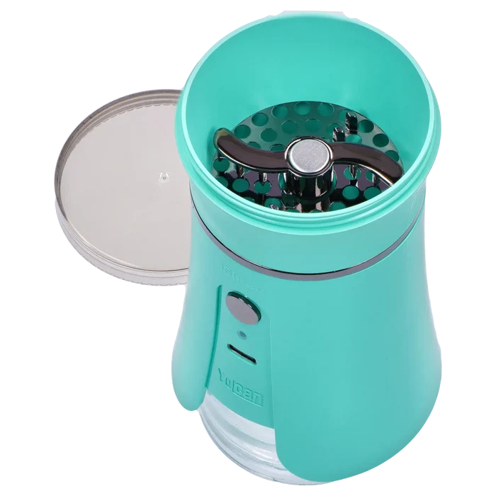 Top-down view of the open Yocan iShred Electronic Grinder – Green showing its teal chamber, silver lid beside it, and black three-prong shredding blade.