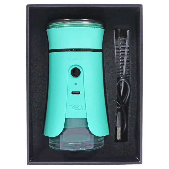 Top-down view of the green Yocan iShred Electronic Grinder seated in black foam packaging with a USB cable and cleaning brush alongside.